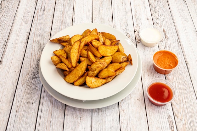 Gran porción de papas fritas cortadas en gajos con salsas variadas para mojar