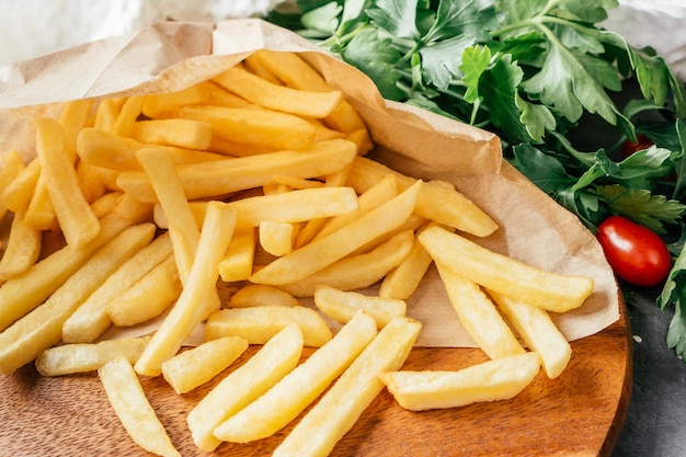 Gran porción de papas fritas en papel artesanal con tomates cherry y perejil verde, sobre superficie de madera