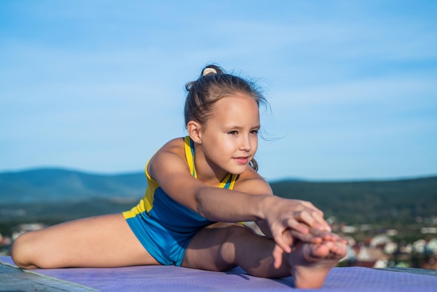 Gran progreso salud y fitness gimnasia niña adolescente feliz sobre fondo de cielo niño tiene cuerpo flexible niño en ropa deportiva concepto de entrenamiento de estiramiento y calentamiento felicidad infantil