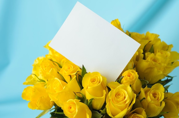 Foto un gran ramo de delicadas rosas amarillas con una tarjeta de felicitación blanca sobre un fondo azul ondulado