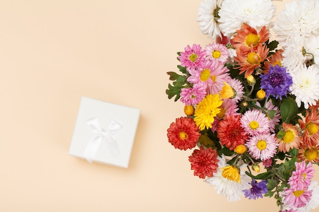 Gran ramo de flores de colores diferentes y caja de regalo blanca sobre fondo beige. Vista superior. Concéntrese en las flores.