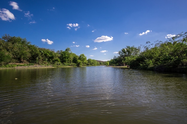 Foto gran río rodeado de árboles y colinas con un cielo azul.