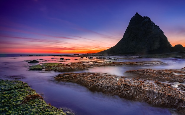 Gran roca en el mar con un pintoresco amanecer en el fondo