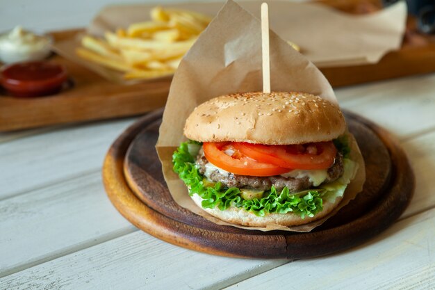 gran sabrosa hamburguesa en una mesa de madera y papas fritas. Deliciosa hamburguesa con ternera, tomate, queso y lechuga.