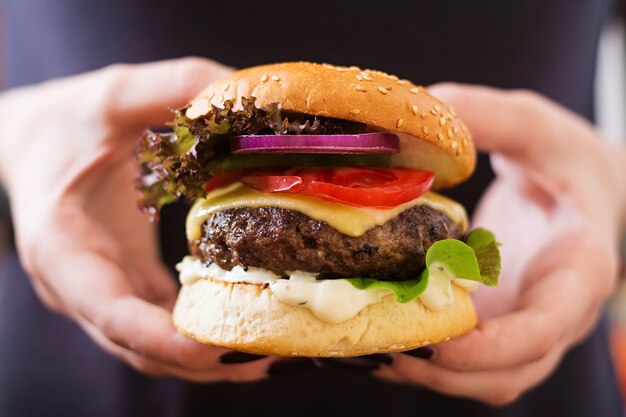 Gran sándwich - Hamburguesa hamburguesa con carne, queso, tomate y salsa tártara en manos femeninas