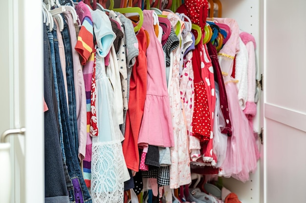 Gran selección de ropa infantil de colores brillantes para una niña colgada en un armario, en perchas.