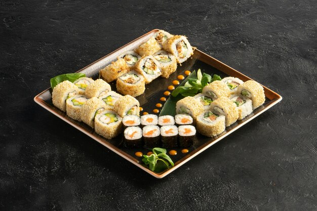 Gran set de sushi maki con un variado surtido de rollos japoneses en un plato cuadrado sobre una mesa de piedra negra