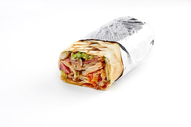 Gran shawarma con carne y verduras, envuelto en papel de aluminio sobre un fondo blanco. Primer plano, enfoque selectivo