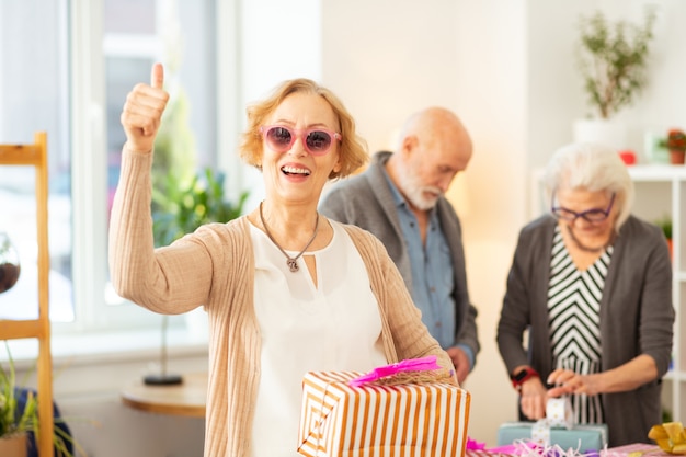 Gran sorpresa. Mujer de edad alegre sonriendo mientras sostiene una caja presente en sus manos