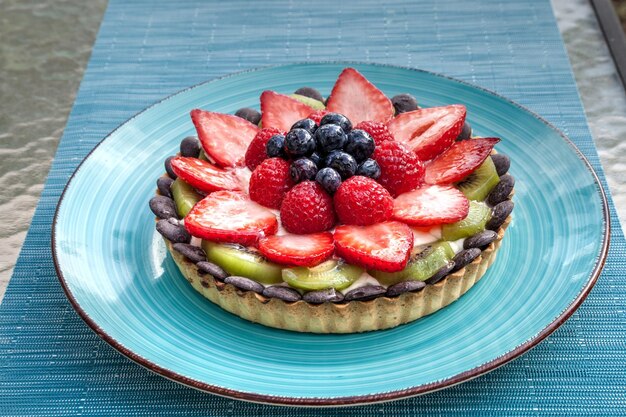 Foto gran tarta de frutas con bayas, incluidas las fresas rojas, las bayas azules, las frambuesas rojas y el kiwi