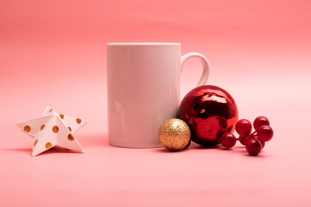 Gran taza de café con leche con adornos navideños a su alrededor sobre fondo de color rosa