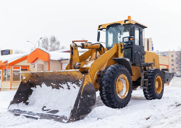 Un gran tractor amarillo quita la nieve de la carreteraLimpieza de carreteras en la ciudad de la nieve en invierno