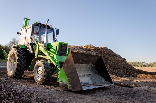 Un gran tractor con un balde se encuentra junto a un montón de residuos de producción de basura reciclado Cielo azul claro en un día soleado