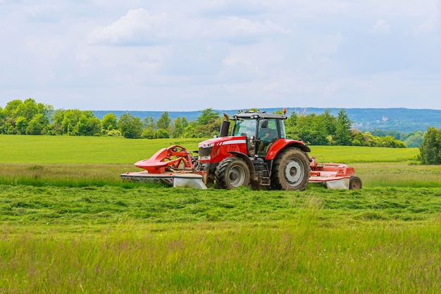 Un gran tractor rojo con dos segadoras corta la hierba verde en un silo.