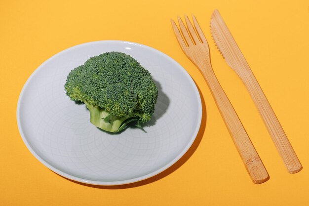 Gran trozo de brócoli en un plato y tenedor y cuchillo de bambú sobre un fondo amarillo