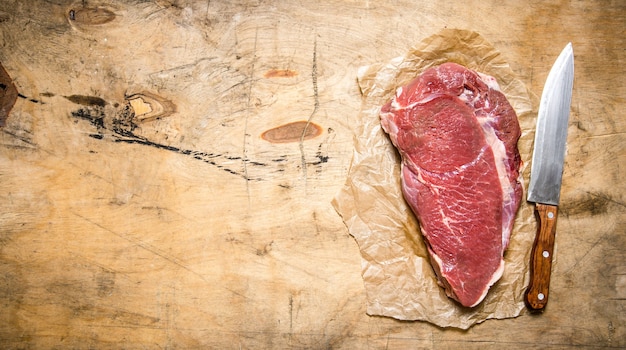 Un gran trozo de carne cruda con un cuchillo de carnicero en el papel.