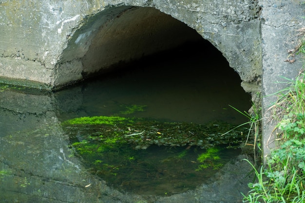 Una gran tubería de hormigón para desviar el río por debajo de la carretera Fugas de agua sucia de grandes tuberías de hormigón Aguas residuales sucias de la tubería contaminación ambiental Problema ambiental