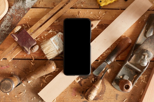 Gran variedad de equipos en la mesa de madera muchas herramientas en el teléfono inteligente de la mesa con pantalla en blanco en el espacio de copia del taller de carpintería para publicidad o texto promocional