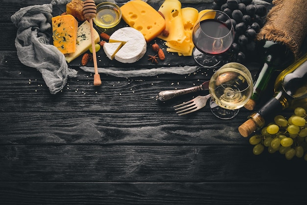 Una gran variedad de quesos queso brie gorgonzola queso azul uvas miel nueces vino tinto y blanco en una mesa de madera Vista superior Espacio libre para texto