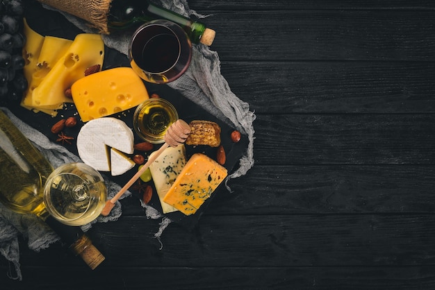 Una gran variedad de quesos queso brie gorgonzola queso azul uvas miel nueces vino tinto y blanco en una mesa de madera Vista superior Espacio libre para texto