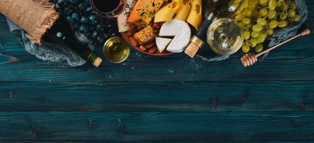 Una gran variedad de quesos, vino, miel, nueces y especias en una mesa de madera azul Vista superior Espacio libre para texto