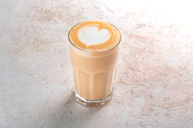 Foto gran vaso de capuchino o café con leche con espuma y un patrón de corazón sobre una mesa blanca de piedra. taza de café estilo minimalista