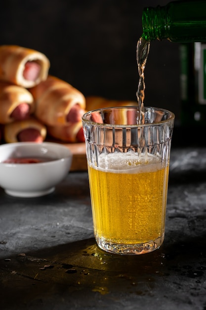 Un gran vaso de cerveza light y salchichas en la masa con salsa.