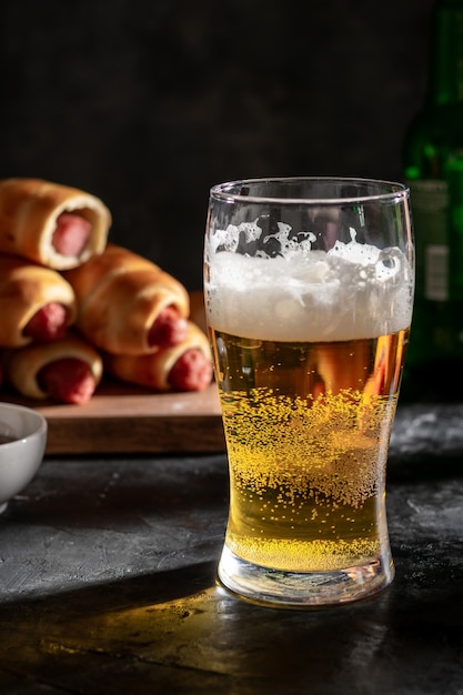 Un gran vaso de cerveza light y salchichas en la masa en el tablero