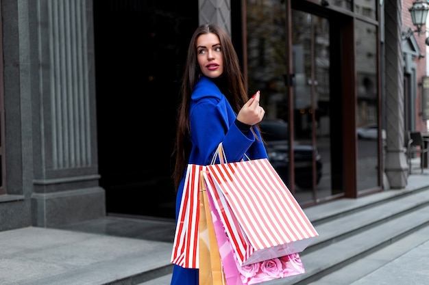 Gran venta. Mujer de moda joven hermosa con bolsas de la compra junto a la ventana de la tienda llamando a teléfonos inteligentes, tonos. mujer de compras, divertido, teléfono