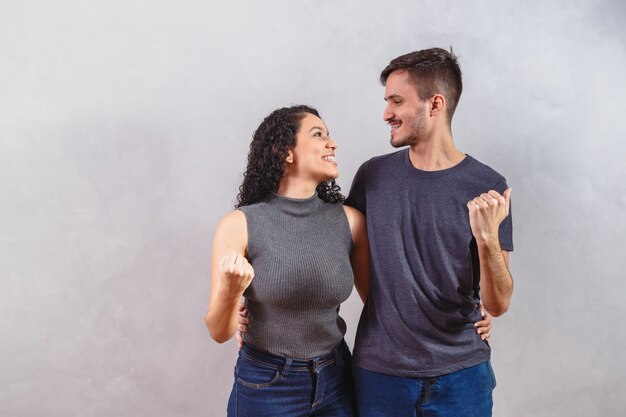 Gran victoria. Feliz pareja interracial regocijándose del éxito, celebrando la victoria con los puños levantados, exclamando con alegría