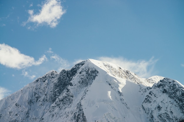 Gran vista a la cima alta de la montaña nevada con nubes bajas bajo cirros en el cielo. Nubes bajas en grandes montañas cubiertas de nieve con pináculo agudo bajo el sol. Pico puntiagudo de nieve blanca a la luz del sol.