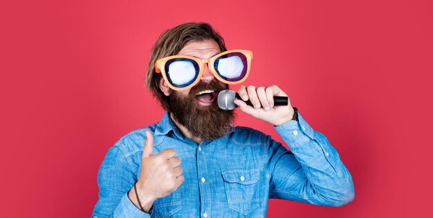 Gran voz brutal hipster caucásico en gafas de fiesta cantante de karaoke chico sin afeitar con pelo largo arreglado barbería y peluquero hombre cantar música en micrófono hombre barbudo divertido con micrófono