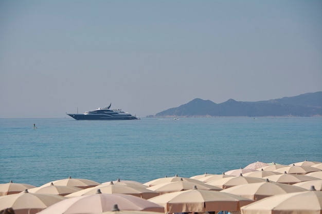 Gran yate amarrado frente a las hileras de sombrillas en la playa de Cerdeña: símbolo de vacaciones y ostentación de riqueza.