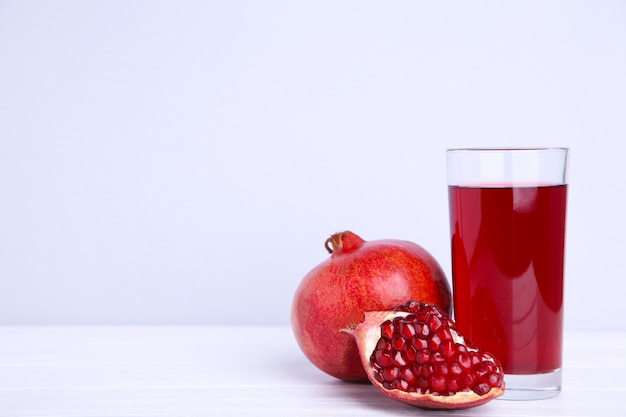 Granada madura y vidrio de jugo de frutas sobre fondo gris