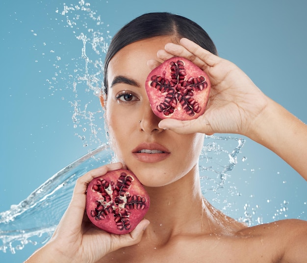 Granatapfel-Hautpflege- und Schönheitsfrau mit Wasserspritzer im blauen Studio-Mock-up für gesunde Wellness- und Hautglanzwerbung Junge Frau mit Vitamin-C-Früchten für Marketing-Mockup für Gesichtsprodukte