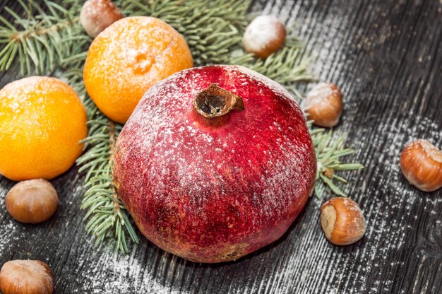 Granatapfel mit Mandarinen, Nüssen und Zweig des Weihnachtsbaums auf dem hölzernen Hintergrund. Weihnachtskarte.