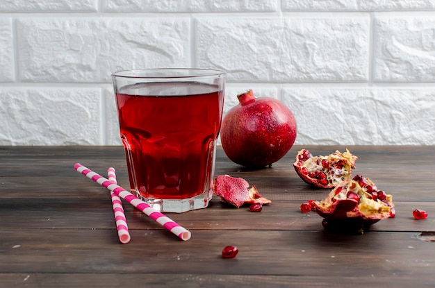 Granatapfelsaft im Glas und Granatäpfel auf dunkler alter Holzoberfläche