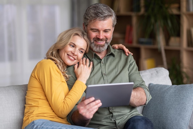 Grande aplicativo feliz cônjuges de meia-idade usando tablet digital juntos em casa