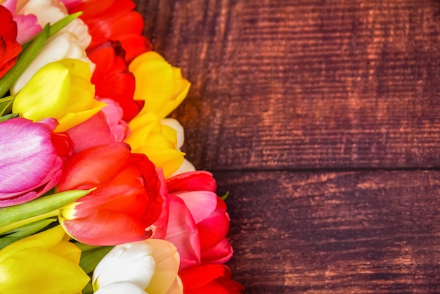 Grande buquê brilhante de tulipas coloridas em tábuas de madeira de cor marrom escuro.