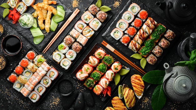 Grande conjunto de rolos de sushi de comida asiática e chá tradicional em um fundo de pedra preta