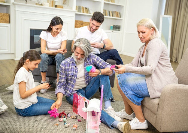 grande e feliz família multigeracional brincando com uma linda garotinha olhando para uma nova casa de bonecas