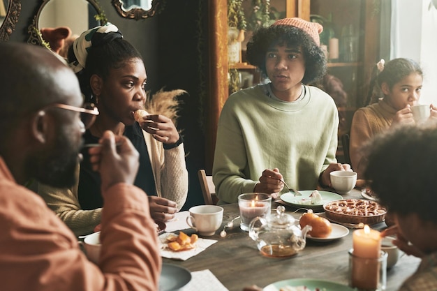 Grande família africana sentada à mesa juntos bebendo chá e comendo torta