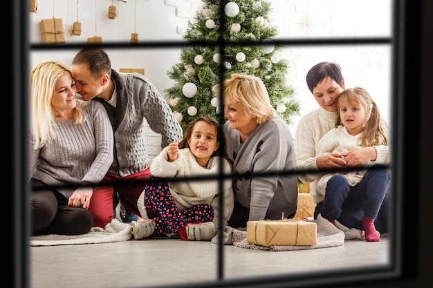 Grande família com três filhos comemorando o Natal em casa. Jantar festivo na lareira e na árvore de Natal. Pai e filhos comendo na lareira no quarto decorado. Vela de coroa de advento de iluminação infantil.