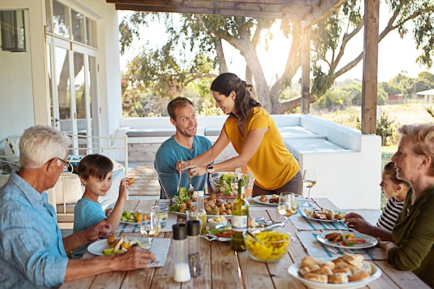 Grande família comendo e comendo com relaxamento ao ar livre no pátio com conversação ligação e refeição saudável no verão pais avós e crianças na mesa de jantar no quintal de casa com conversa ou diversão