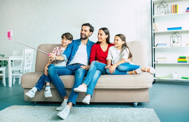 Grande família feliz e engraçada fazendo selfie no telefone inteligente com bastão de selfie no sofá em casa