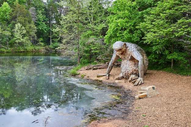 Foto grande gigante amigável sentado na cobertura morta na margem do lago, olhando tristemente para a água suja da lagoa