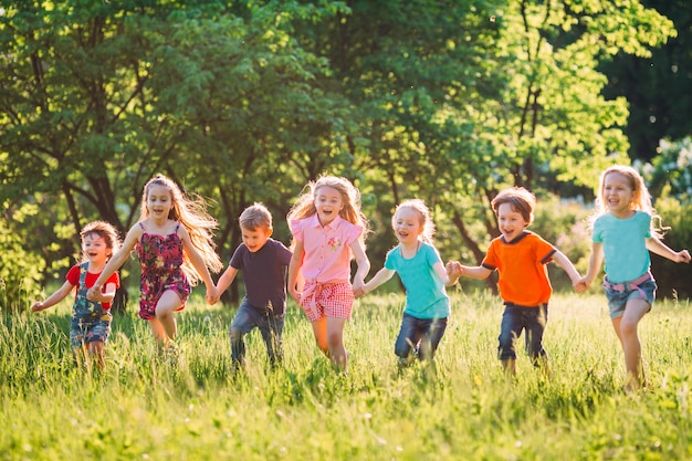 Grande grupo de crianças, amigos meninos e meninas correndo no parque no dia de verão ensolarado em roupas casuais.