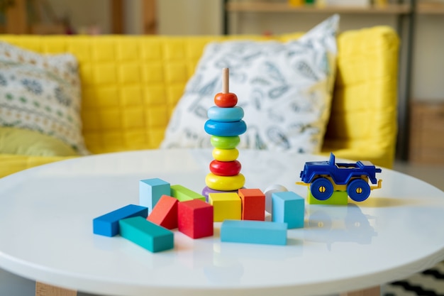 Grande grupo de pequenos cubos de madeira de várias cores, caminhão de plástico e pilha de seções azuis, amarelas e vermelhas do brinquedo na vara na mesa
