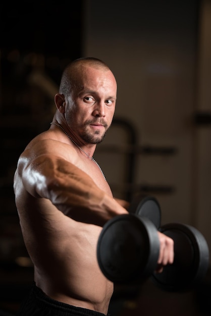 Grande homem de pé forte no ginásio e exercitando ombros com halteres muscular Atlético Bodybuilder exercício modelo no centro de fitness