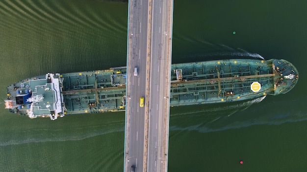 Grande navio-tanque de carga geral que passa sob uma ponte com vista aérea de tráfego pesado